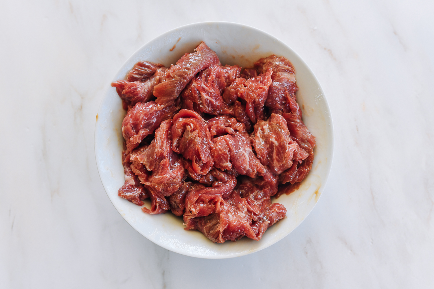 marinated sliced flank steak in white bowl