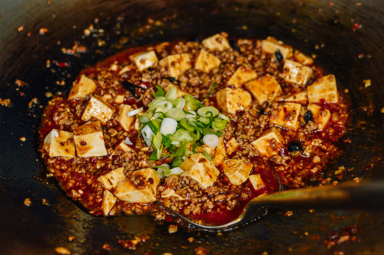 Adding scallions to mapo tofu, thewoksoflife.com